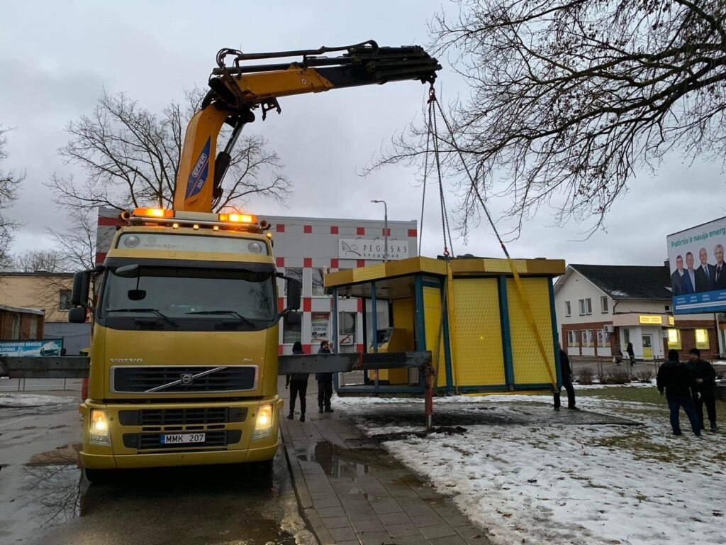 Krano sunkvežimis kelia geltoną kioską miesto gatvėje